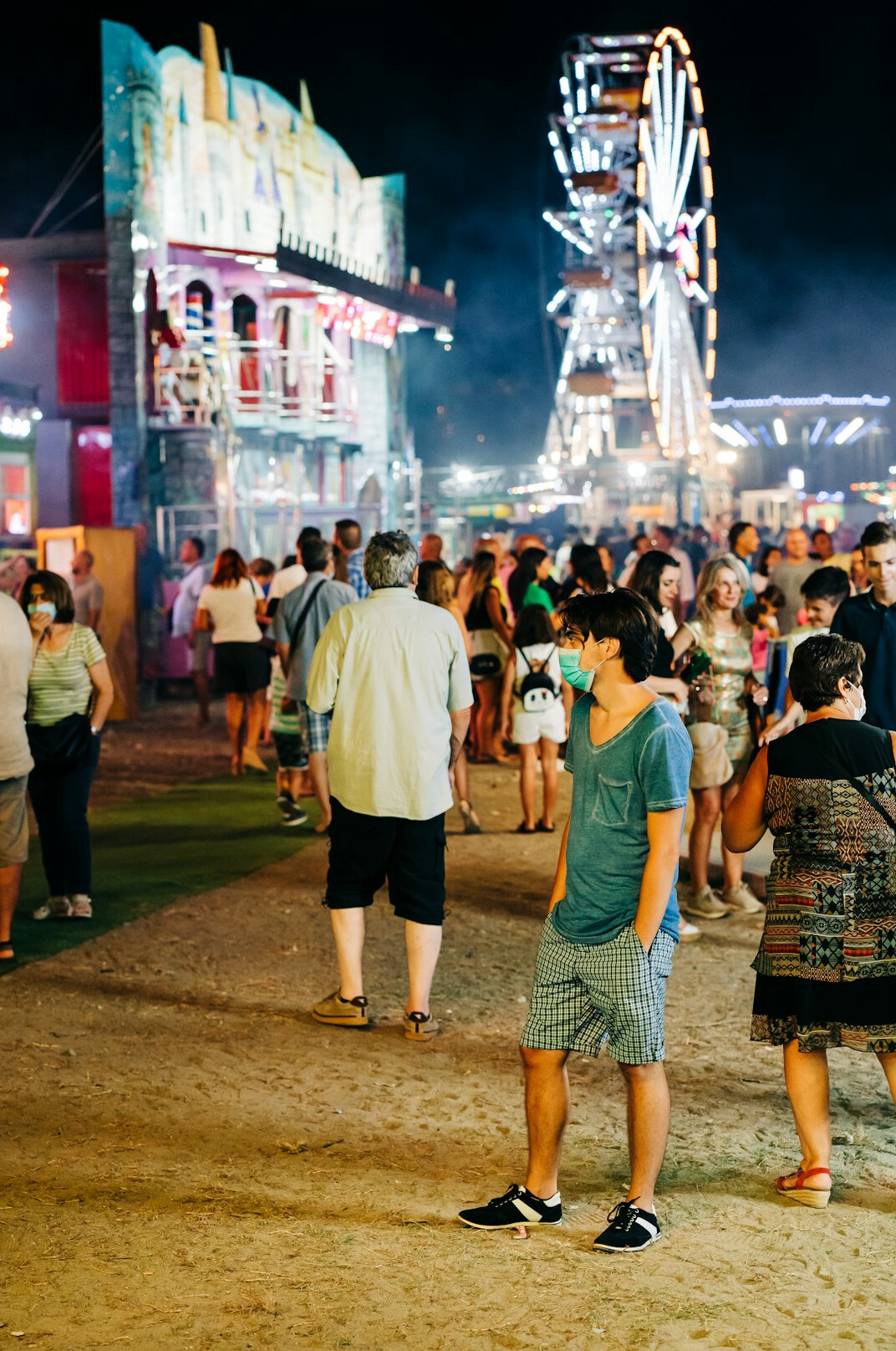 Visitors queueing at the entrance of a lit amusement park in the evening